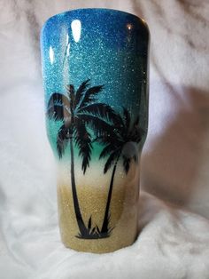 a blue and white coffee cup with palm trees painted on the side, sitting on a bed