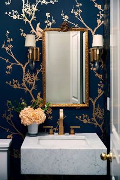 a bathroom with blue walls, gold accents and a white marble sink under a large mirror