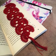 an open book with red crocheted lace on it next to a tassel