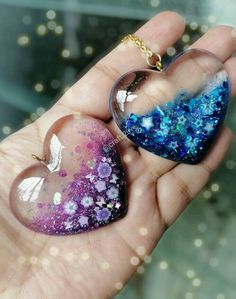 two heart shaped glass pendants in the palm of someone's hand, one with blue and purple flecks on it