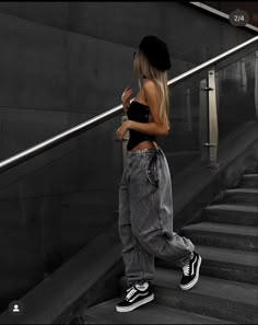 a woman in black top and jeans walking down stairs with her hand on her hip