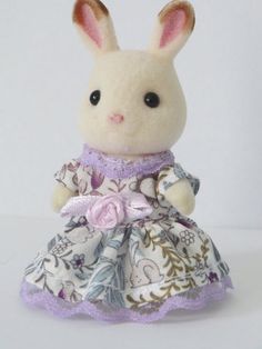 a white stuffed animal wearing a dress with flowers on it's chest and ears