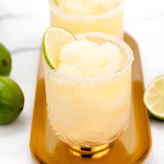 two glasses filled with ice and limes sitting on a tray next to some limes