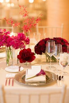 the table is set with red flowers and place settings