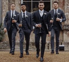 three men in suits and ties are walking with wine glasses on their feet while one man is holding a drink