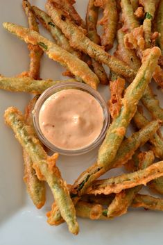 some fried food on a white plate with a small dip in the middle and dipping sauce