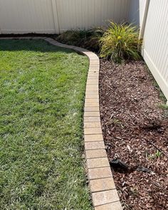 a brick walkway in front of a white fence with grass and mulch on the ground