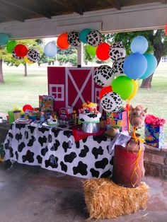 a cow themed birthday party with balloons, cake and other items on the table under an awning