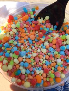 a plastic bowl filled with lots of colorful candies and a black spoon in it