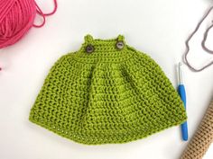 a crocheted green hat with buttons and yarn next to it on a white surface