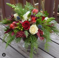 a vase filled with flowers and greenery on top of a wooden table