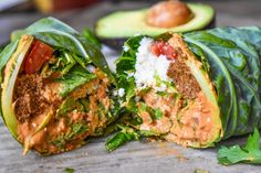 a wrap filled with lettuce and meat on top of a wooden table next to an avocado