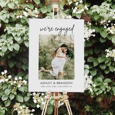 an easel with a sign on it that says we're engaged in front of some flowers