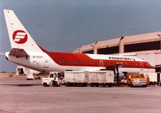 a red and white plane parked in front of an airport terminal with trucks around it