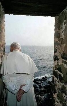 the man is looking out at the ocean from inside an old stone structure with water in the background