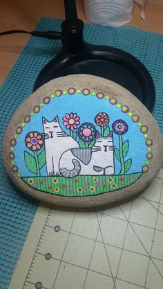 a rock with two cats painted on it sitting on top of a table next to a pair of scissors