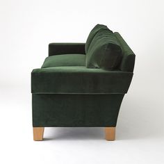 a green velvet couch with two pillows on it's arms and legs, against a white background