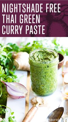 a jar filled with green curry paste on top of a table next to garlic and herbs