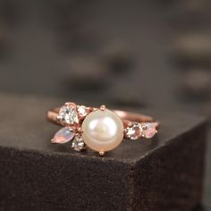 a pearl and diamond ring sitting on top of a piece of black stone block,