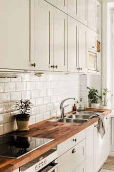 a kitchen with white cabinets and wooden counter tops, along with potted plants on the window sill