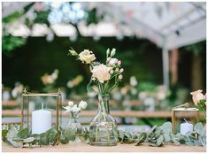 flowers in vases and candles are sitting on a table with greenery around them