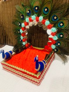 an elaborately decorated peacock sitting on top of a red blanket next to a pillow