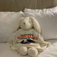 a white stuffed rabbit sitting on top of a bed next to pillows and pillow cases