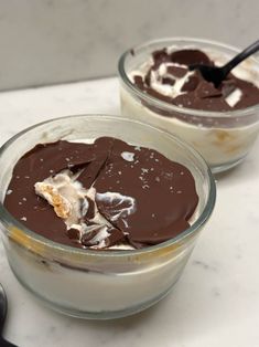 two desserts with chocolate and marshmallow toppings in glass bowls on a marble countertop