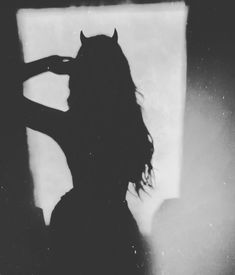 the silhouette of a woman brushing her hair in front of a window with light coming through it