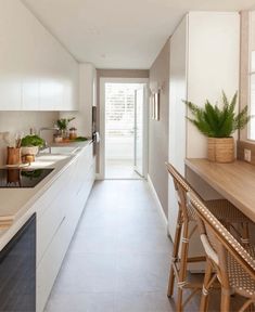 a long narrow kitchen with white cabinets and counter tops, along with wooden bar stools