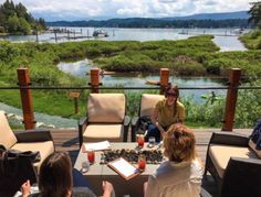 people sitting around a table with drinks on it looking out at the water and land