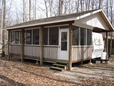 a small white cabin in the woods with a porch and covered veranda area next to it