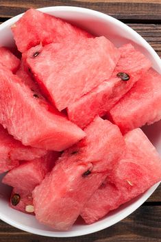 a white bowl filled with watermelon slices on top of a wooden table