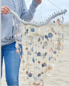 a woman holding up a mobile made out of seashells