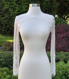 a white dress with sheer sleeves on a mannequin stand in front of some bushes