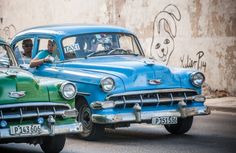 two old cars parked next to each other in front of a wall with graffiti on it