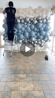 a man standing on a stepladder in front of a giant balloon wall with silver and white balloons