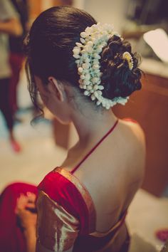 a woman with flowers in her hair sitting on the floor next to a table and another person standing behind her