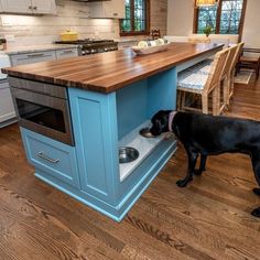 a black dog eating food out of a dishwasher in a kitchen with an island