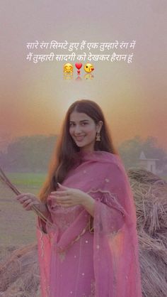 a woman in a pink sari standing next to hay bales with the sun setting behind her