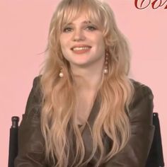 a woman with long blonde hair sitting in a black chair and smiling at the camera