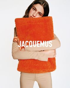 a woman holding an orange pillow with the word jacquemus on it