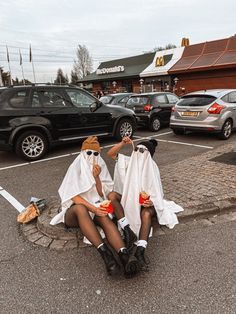 two women dressed in white sitting on the ground eating hotdogs and drinking soda