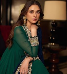 a woman in a green dress sitting on a red couch wearing gold jewelry and earrings