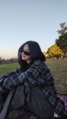 a woman sitting on top of a purple and black blanket next to a park with trees