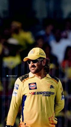 a man in yellow shirt and hat standing next to a fence with people watching from the stands