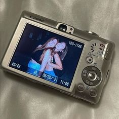 a digital camera with a woman on it's screen sitting on a white sheet