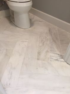 a white toilet sitting inside of a bathroom next to a shower stall and tiled floor