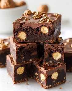 a stack of chocolate brownies sitting on top of a white table next to some nuts