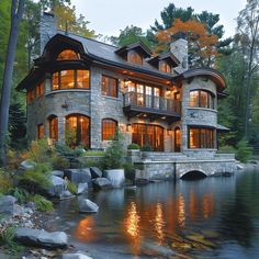 a large house sitting on top of a lush green hillside next to a lake in front of a forest